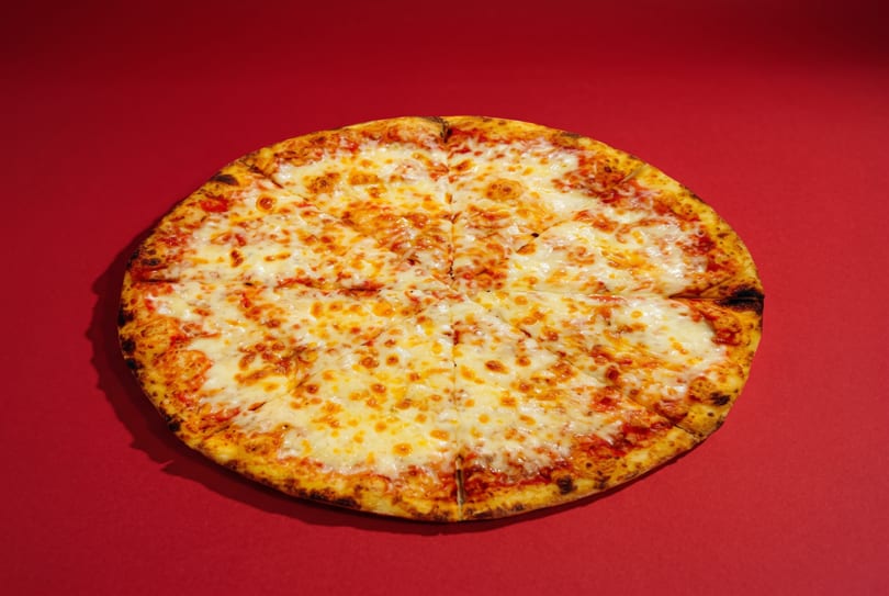 A whole cheese pizza, cut into slices, on a vibrant red background.