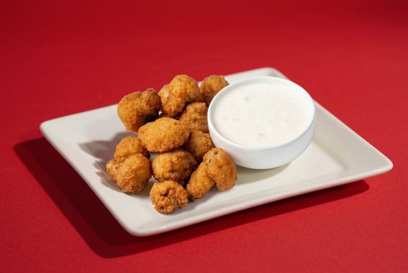 Golden-brown fried mushrooms on a white rectangular plate with a side of creamy ranch dip.
