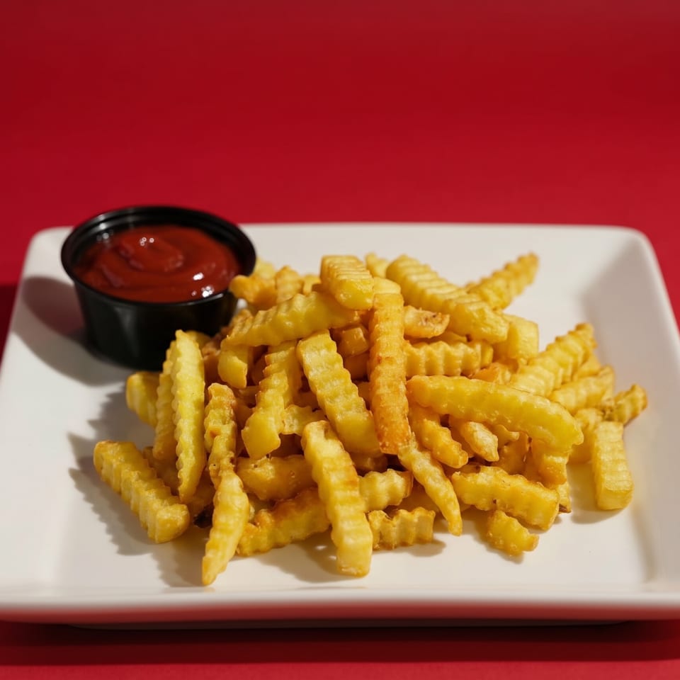 A white rectangular plate holds a pile of golden crinkle-cut fries and a small cup of ketchup.